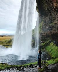 Man standing on rock against waterfall