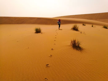 Man walking on sand dune in desert against clear sky