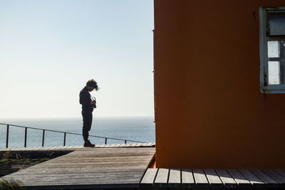 Man looking at camera while standing on pier by sea against sky