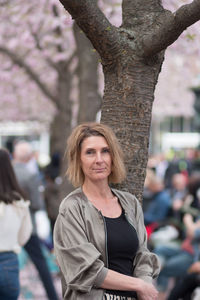 Portrait of woman standing against tree trunk