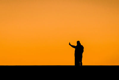 Silhouette of man standing against orange sky