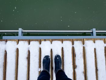 Personal perspective of female black boots standing on a wooden pontoon covered in snow