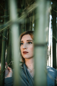 Young woman looking away while standing by bamboos