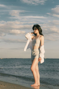 Young woman standing at beach. short jeans, white blouse and black hair