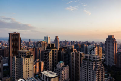 Modern buildings in city against sky during sunset