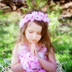 Cute girl praying while wearing floral crown on field