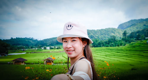 Portrait of smiling young woman in field against sky