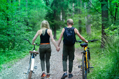 Rear view of people on road amidst trees in forest