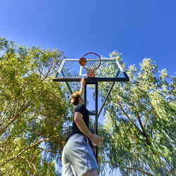 Low angle view of man putting ball in basketball hoop against clear sky