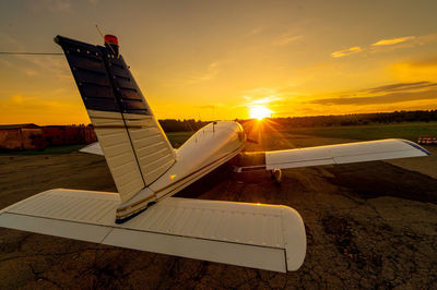 Airplane on airport runway against sky during sunset