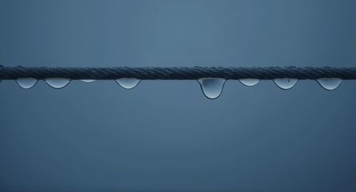 Close-up of water drops on metal wire against sky