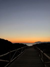 Bridge over calm sea against clear sky during sunset