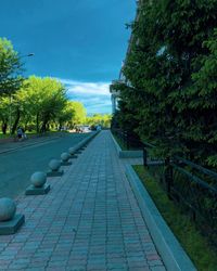 Empty footpath in park against blue sky