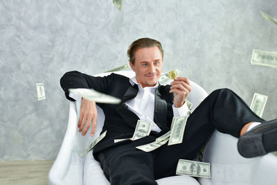 Businessman holding coin while sitting against wall on chair