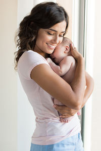 Happy woman with baby girl standing against wall