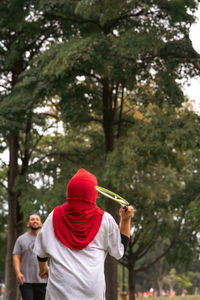 Asian family playing badminton in the park. woman in hijab, view from behind.