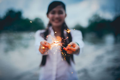 Young woman holding sparkler at night