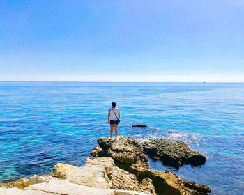 Rear view of man standing on rock against sea