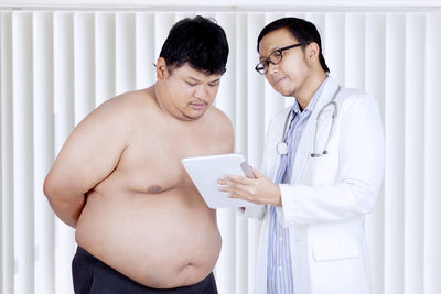 Doctor with shirtless male patient discussing over digital tablet in hospital