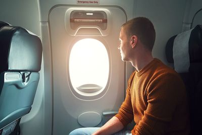 Young man looking through window while traveling in airplane