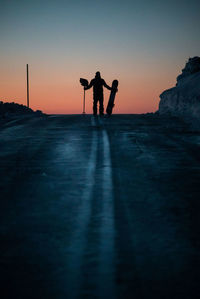 Silhouette man standing with snowboard against sky during sunset