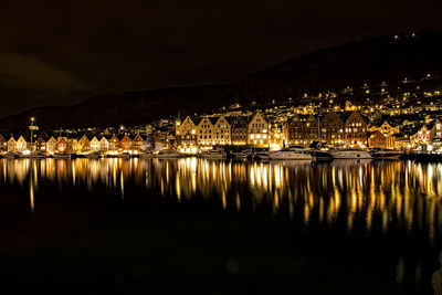 Illuminated buildings by lake against sky at night