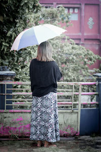 Rear view of woman with umbrella standing against building