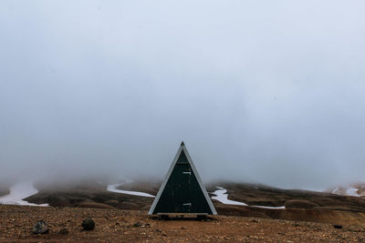 Triangle shape outhouse on ground during foggy weather