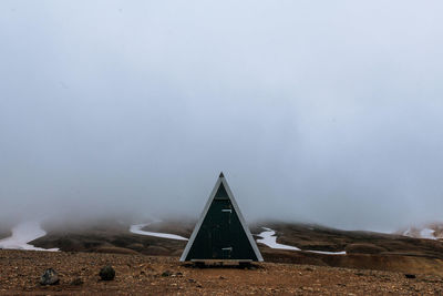 Triangle shape outhouse on ground during foggy weather