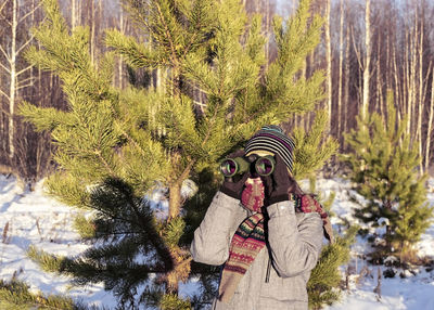 Young woman birdwatcher looking through binoculars in winter snowy pine forest. ecology, ornithology