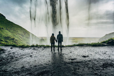 Rear view of couple holding hands against waterfall