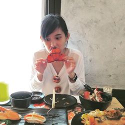 Woman looking away while eating lobsters at table against wall