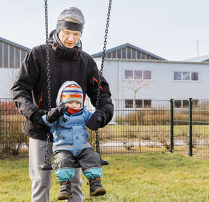 Grandfather assisting granddaughter in swinging against houses