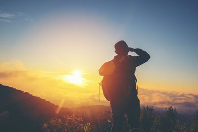Man photographing on mountain against sky at sunset