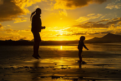 Silhouette father and son at beach against sky during sunset