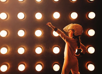 Rear view of girl standing against lighting equipment
