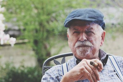 Portrait of senior man smoking cigar while sitting in yard