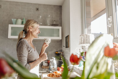 Happy woman at home in kitchen looking out of window