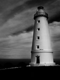 Lighthouse on beach against cloudy sky