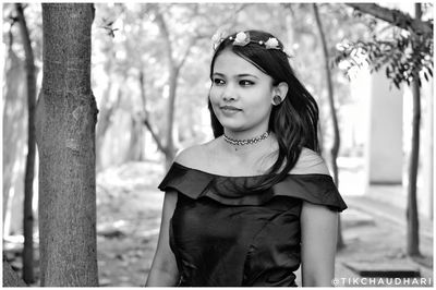 Portrait of smiling young woman standing against tree trunk