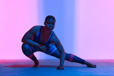 Portrait of woman doing stretching exercise in front of wall