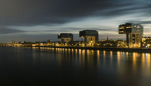 Illuminated buildings by river against sky at dusk