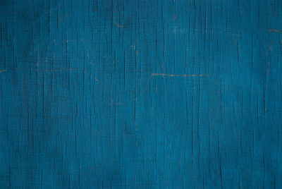 Dark blue-green texture of faded plywood wall with cracks, scratches and stains
