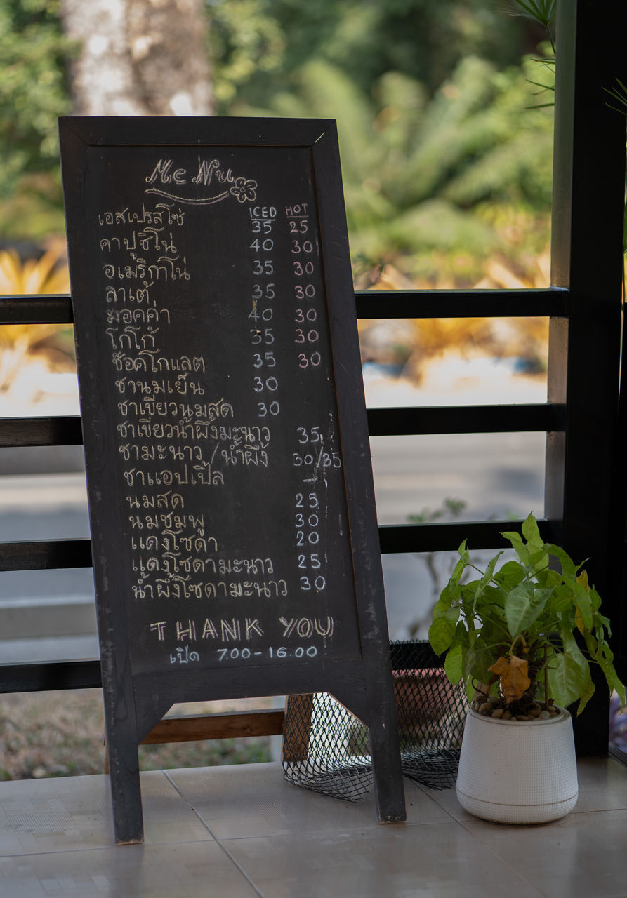 menu, text, plant, blackboard, communication, nature, no people, table, potted plant, food and drink, green, board, flower, food, western script, outdoors, houseplant, day, seat, restaurant, architecture, cafe