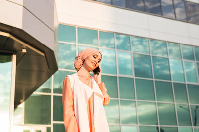 Young woman talking on phone while standing against building