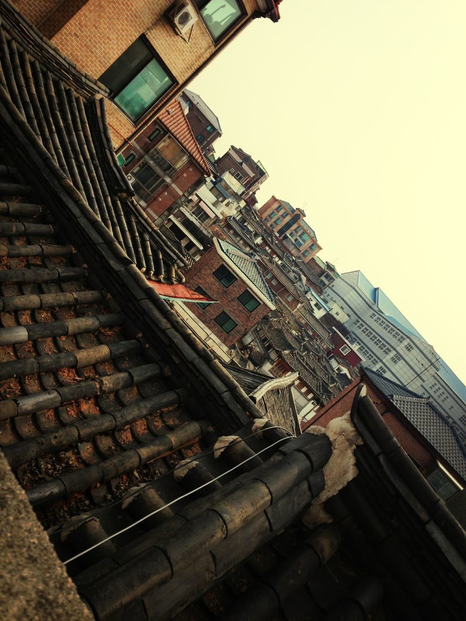 building exterior, architecture, built structure, low angle view, clear sky, roof, building, city, residential building, residential structure, day, sky, tilt, outdoors, sunlight, copy space, no people, roof tile, house, brick wall