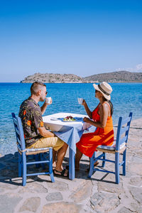 Friends sitting on chair at beach against clear blue sky