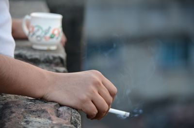 Midsection of man holding cigarette by retaining wall