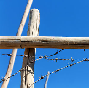 Low angle view of barbed wire fence against blue sky