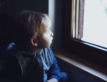 Close-up of cute girl looking through window at home